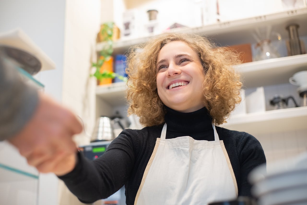 Smiling barista in café, engaging positively with customer, signifying hospitality.